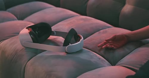 Close up of virtual reality goggles on a velvet couch next to a hand