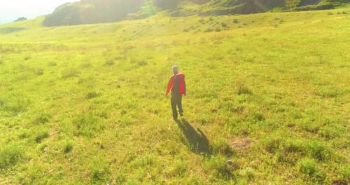 Flight Over Backpack Hiking Tourist Walking Across Green Mountain Field. Huge Rural Valley at Summer