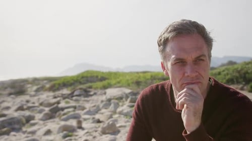 Caucasian man enjoying free time by sea on sunny day sitting and thinking