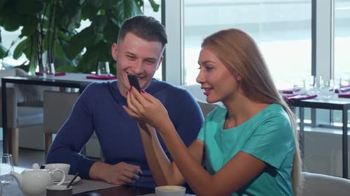 Young Couple Sharing Phone at Restaurant Table