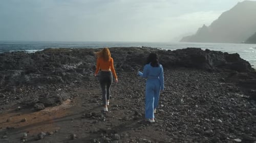 Zwei wunderschöne Freundinnen spazieren am Vulkanstrand im Norden der Kanareninsel entlang
