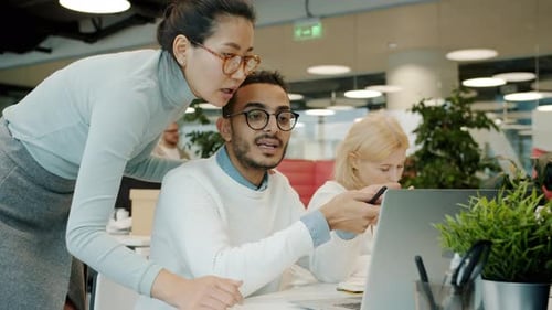 Male and Female Colleagues Talking Looking at Laptop Indoors in Shared Office