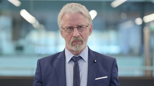 Stern Senior Man Raises Index Finger Indoors