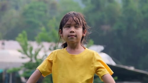 Cute little girl having fun catching rain drops. Kids play in summer rain. Child playing outdoor.