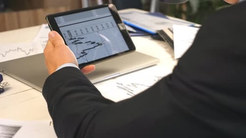 Male Hands of Young Businessman Analyzing Statistical Data Information on a Tablet Pc and Drinking