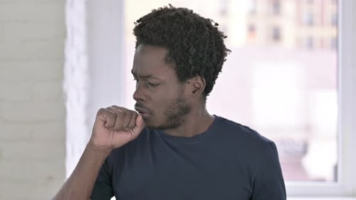 Young Adult Coughing Indoors in Front of Window