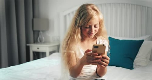 Girl Using Phone Sitting on Bed in Bedroom