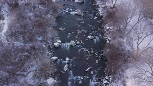 Looking straight down at a river rushing along a valley in winter - zooming out