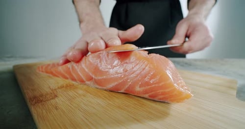 Chef Begins To Cut with a Knife Fish To the Wooden Board. Close Up, Slow Motion