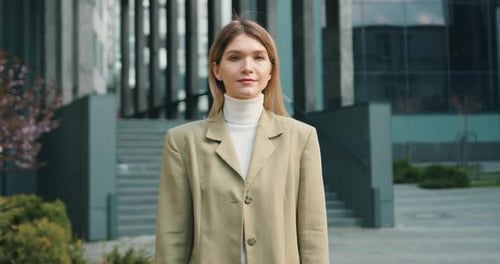 Mujer caucásica mirando a la cámara mientras está de pie fuera del edificio de oficinas.