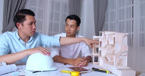 Two Asian Male Architects Working With New Architectural House Model