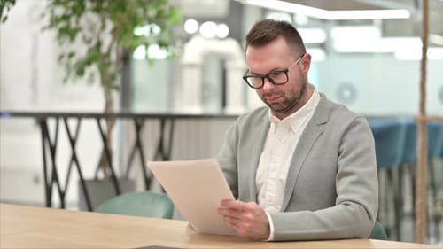 Man Reviews Documents at Table in Office