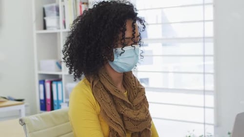 Woman wearing face mask sitting on her desk at office