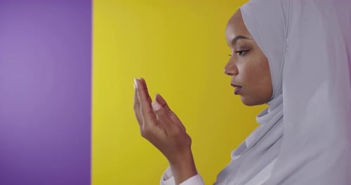 Moderne afrikanische Muslimin betet vor buntem Hintergrund traditionell zu Gott
