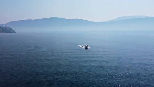 Small boat speeding on Okanagan Lake with smoke from many wildfires covering the hills in the backgr