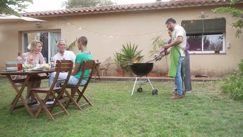 Adult Friends Enjoying Outdoor Summer BBQ at Home Garden Cooking and Having Good Times Together