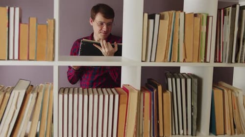 Ein Mann mit Brille liest ein Buch in der Bibliothek hinter den Bücherregalen