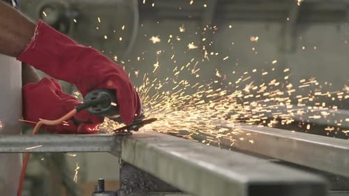 Zeitlupe eines Arbeiters, der eine Metallschleifmaschine benutzt und Funken in einer Metallwerkstatt fliegen