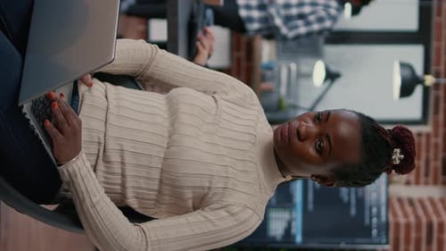 Vertical Video Portrait of African American Programer Sitting Down Coding on Laptop Looking Up and