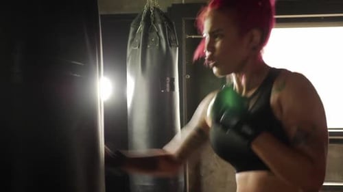Young sporty woman doing boxing training with punching bag at the gym