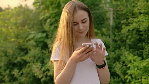 Portrait of a Beautiful Woman Typing on a Mobile Phone in the Park