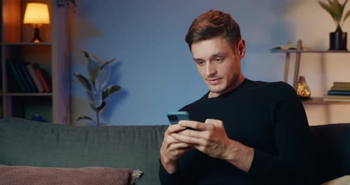 Man Using Smartphone on Couch Shows Surprise