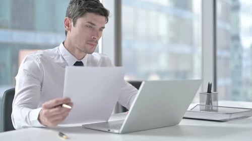 Focused Businessman Reviews Documents in Modern Office