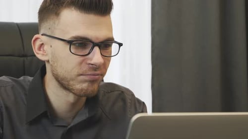 Nahaufnahme eines Mannes, der im Büro mit Brille am Laptop arbeitet