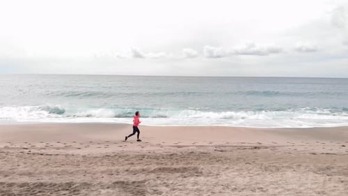 Young woman is jogging on empty beach.