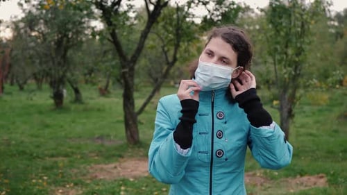 Woman Putting on Surgical Mask in Park