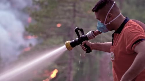 Firefighter Sprays Water on a Forest Wildfire