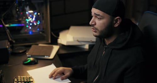 Tired Overworked Male Programmer in a Cap Sweatshirt Works at Night in Dark Room Sleeps in Front of