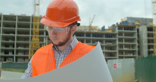 Young Architect or Builder With Hard Hat Holding Blueprint In His Hands in Front of Building Under
