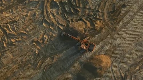 Une excavatrice égalise la surface sablonneuse du chantier au coucher du soleil