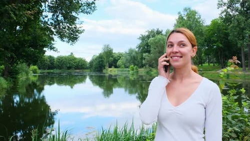Pretty Woman Talking on Mobile Phone on the Background of the Park