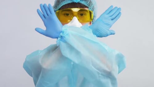 Trabajante en traje de protección con guantes azules y gafas amarillas que muestra la señal de stop con los brazos