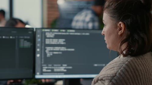 Over Shoulder View of Focused Database Designer Writing Code Looking at Multiple Computer Screens
