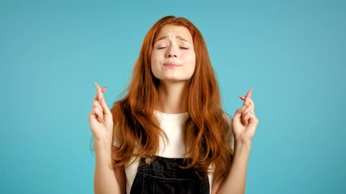 Young Woman Crossing Fingers on Blue Background