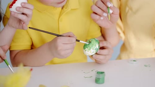 Mother Colouring Easter Eggs with Her Kids in White Room