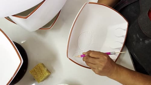 Hands Carefully Carving Design into a White Plate