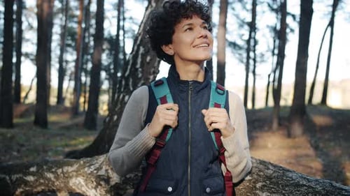 Portrait of Curlyhaired Girl Standing in Forest with Backpack and Looking Around