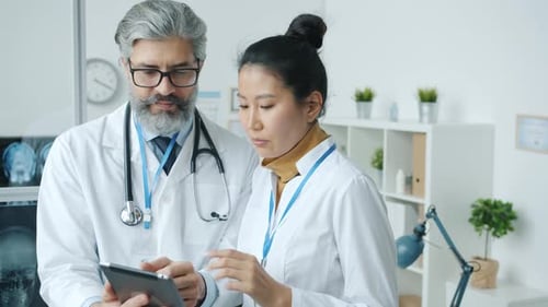Doctors Caucasian Man and Asian Woman Talking and Looking at Laptop Screen in Hospital Office