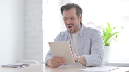 Young Man Celebrating Success on Tablet in Office