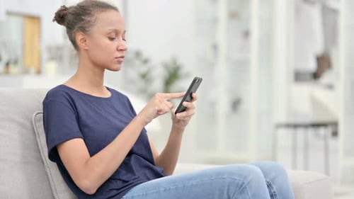 Woman Scrolls Phone Sitting on Sofa Indoors