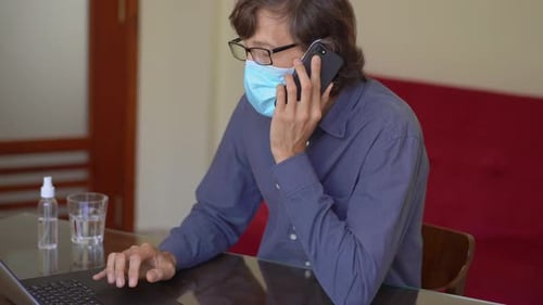 A Young Man Wearing a Face Mask Works From Home During Corona Virus Self Isolation