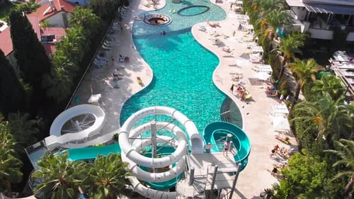 Fly Over a Large Pool with Blue Water and a Lot of Tourists in Hot Weather