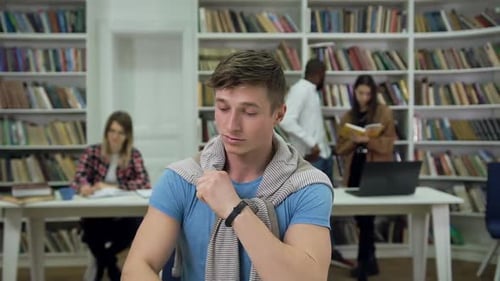 Young Man Looking Aside in the Library and then Writing Notes Into Copybook
