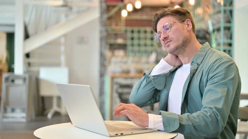Tired Middle Aged Man with Laptop Having Neck Pain in Cafe