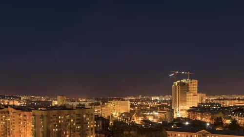 Night Cityscape and Large Tower Cranes Build Multistorey Buildings