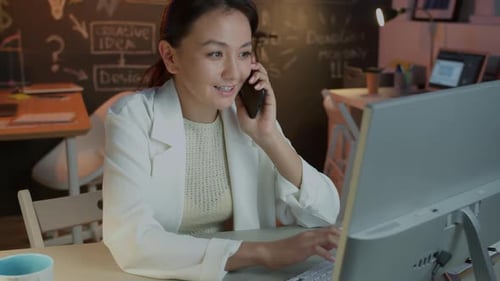 Motivated Businesswoman Speaking on Mobile Phone and Working with Pc Indoors in Dark Office